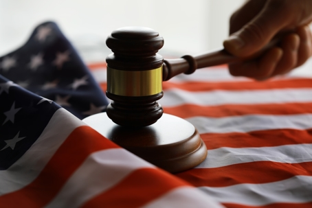 Judge's gavel on the table in focus over an American flag.